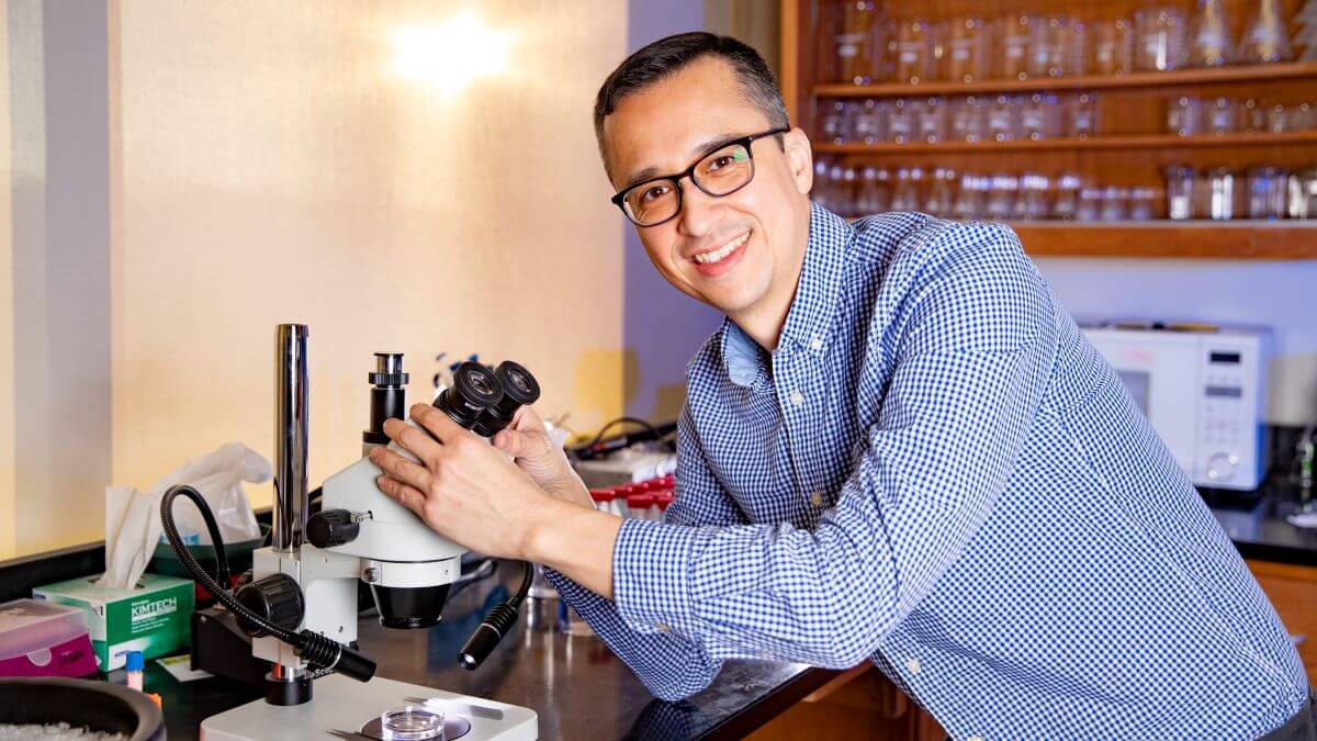 Dr. Ryan Udan leans over a microscope in his research lab.
