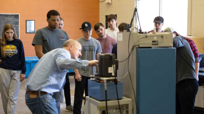Luther Harris and classmates watching Dr. Matt Pierson use a machine during an engineering lab.