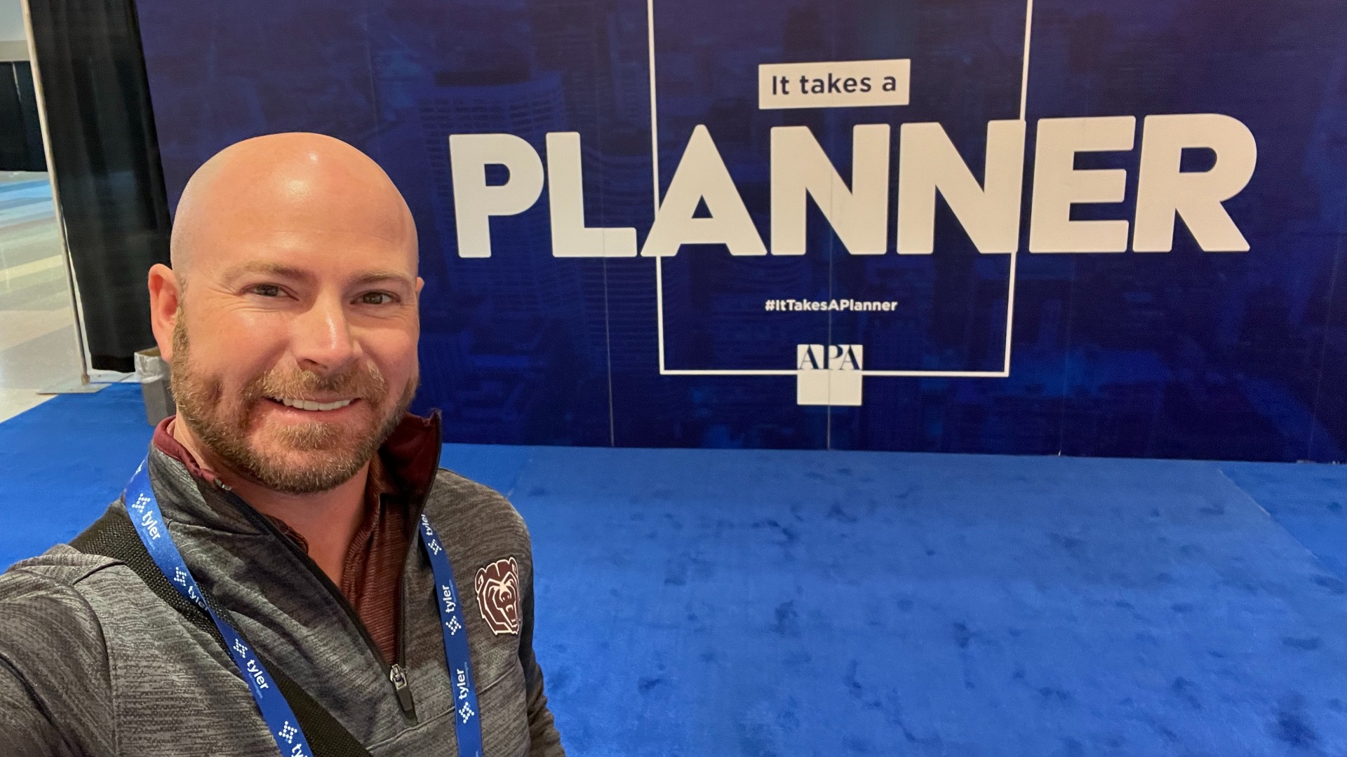 Jason Ray in front of a backdrop with the words "It takes a PLANNER."