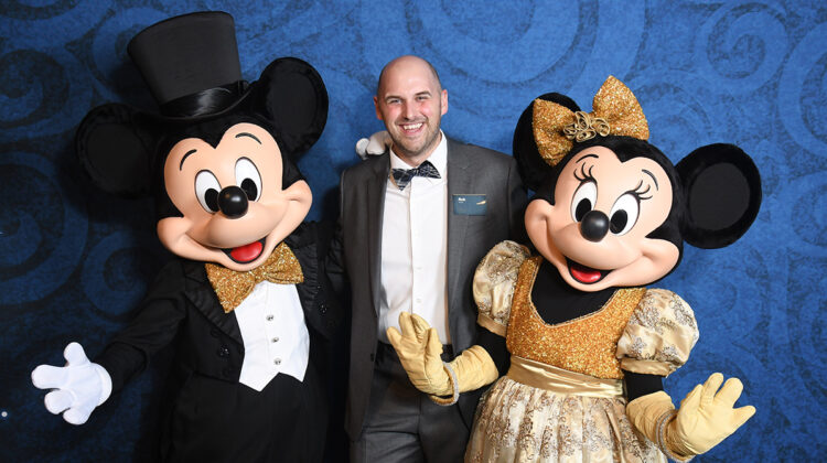 Man in a suit in between Mickey and Minnie Mouse.