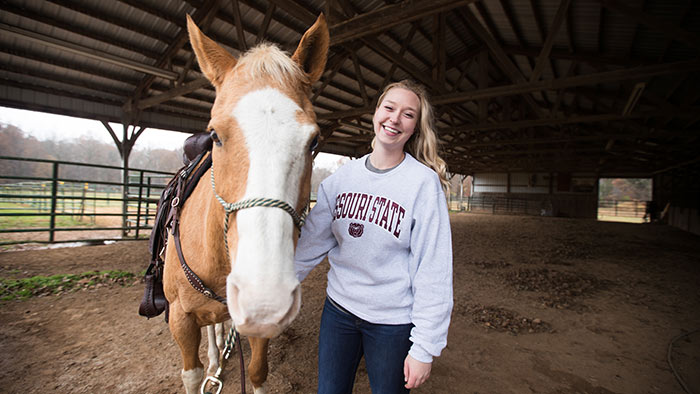 Emily Hrpcha posing next to horse.