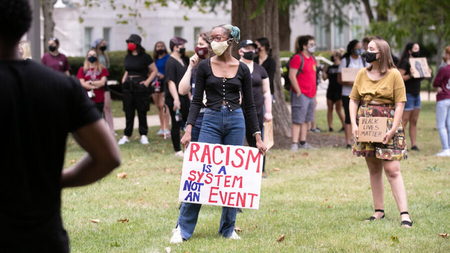 Student holding a sign that says, "Racism is a system not an event."
