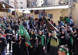 A group of men and women dressed in black, some holding flags, participating in Ashura in Syria in 2017.