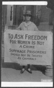 Photograph of Mary Winsor, standing outside, holding a banner that reads: "To Ask Freedom for Women is Not a Crime. Suffrage Prisoners Should Not be Treated as Criminals."