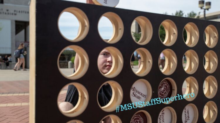 Face peeking through large connect 4 game with MSU checkers.