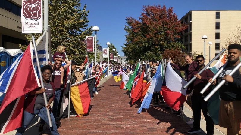 A group of students holding international flags for the Missouri State Bears Football team to walk through at BearFest Village