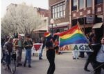 A parade with individuals holding up a GLO sign and pride flag.
