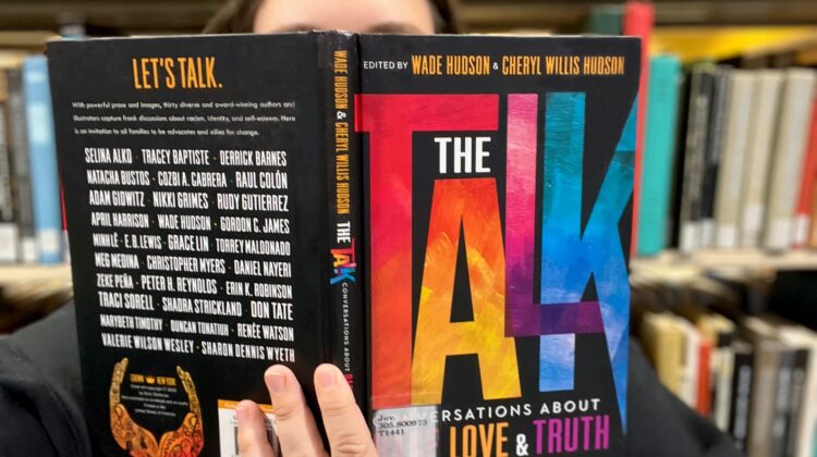 Person hiding behind the book "The Talk: Conversations About Hate, Love and Truth".