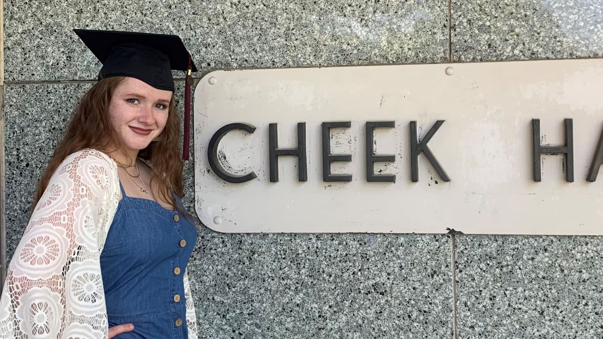 Sabrina Klement stands outside of Cheek Hall. She wears her graduation cap.