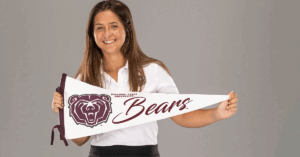 Helena grins as she holds up a Missouri State pennant flag.