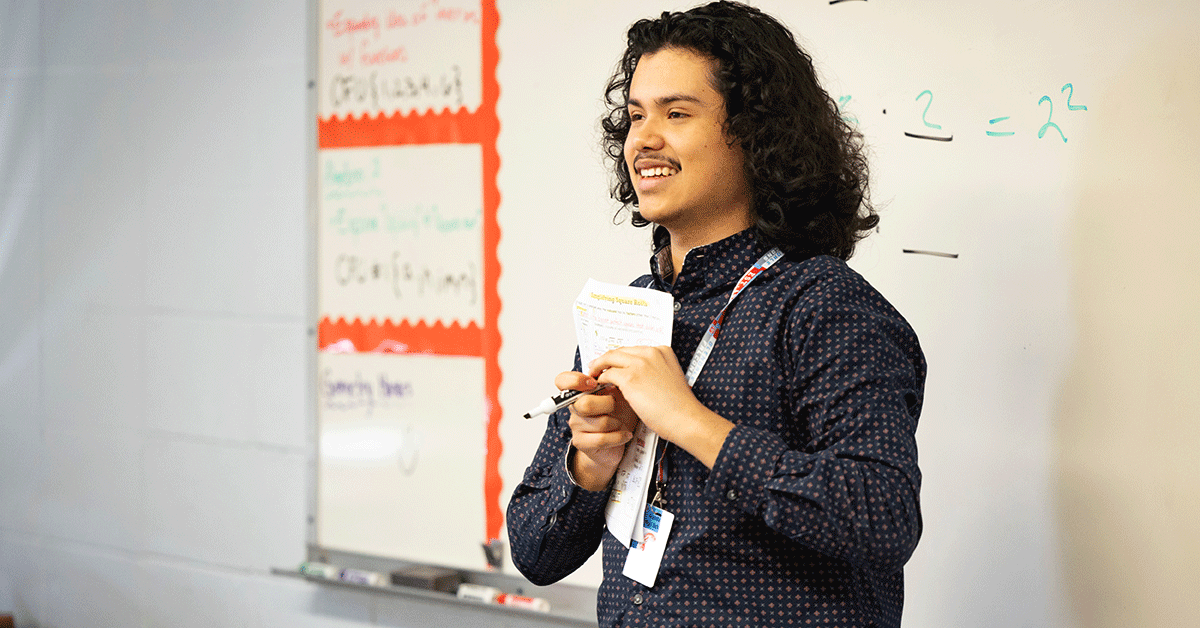Joseeduardo Granados Rodriguez smiles while standing in front of a whiteboard at the front of a classroom.