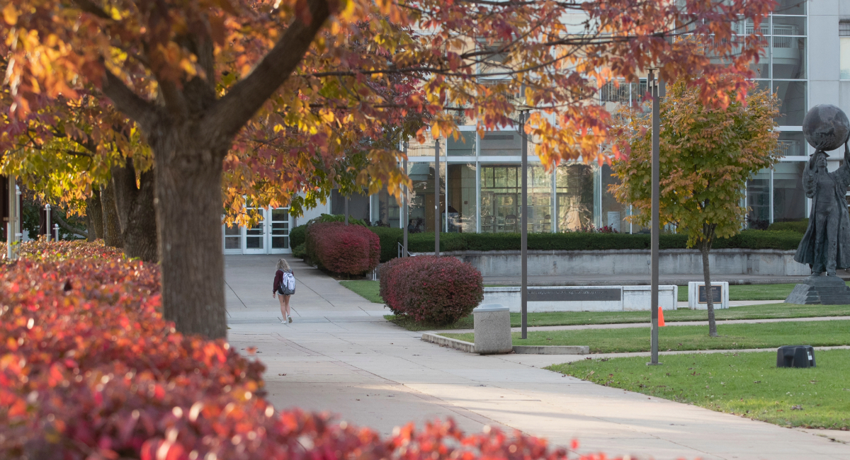 A student walking toward Strong Hall on campus on a fall day.