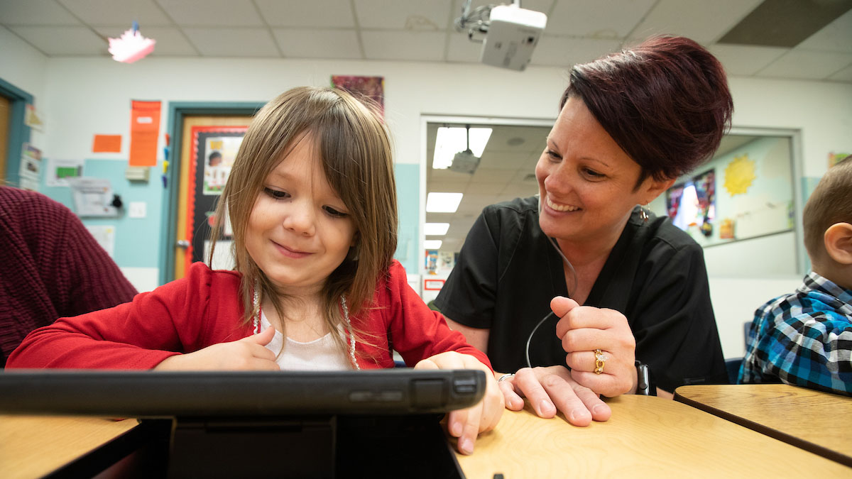 Tara Oetting helps a young girl on a screen device