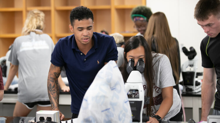 students look through a microscope in lab