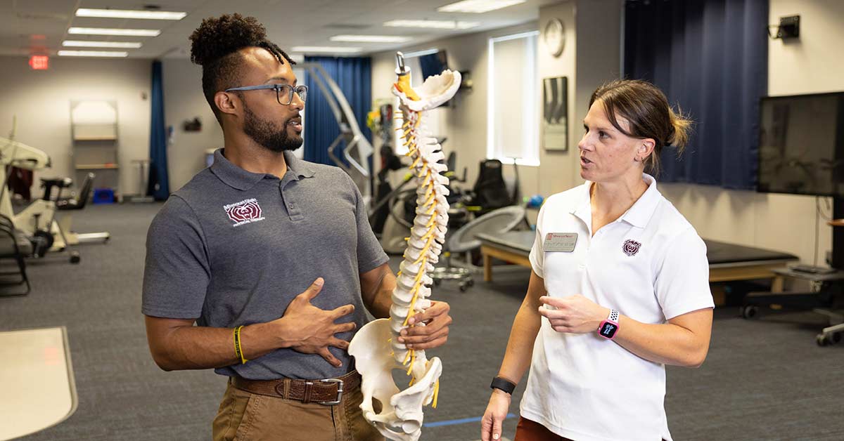 William Smith talks with physical therapy faculty member Dr. Kim Ennis during a lab activity. Smith is holding up a model of the human spine.