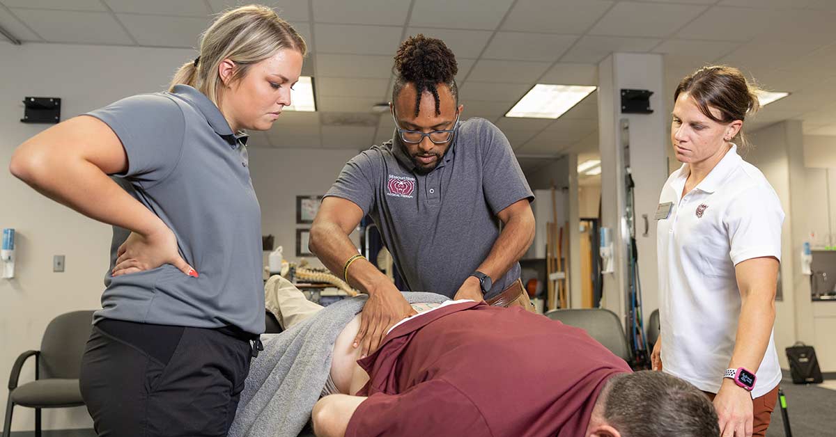 Three physical therapists, including William Smith, do a spine exam on a patient.