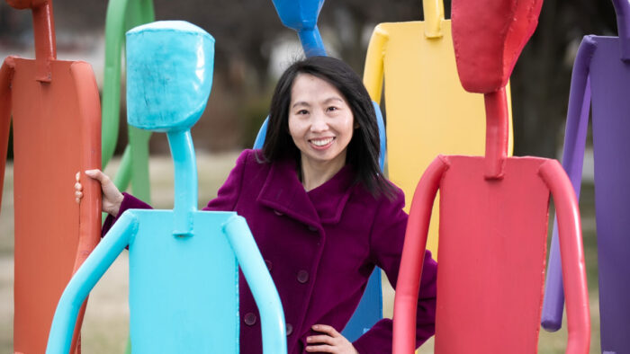 Xiaomin Qiu stands among colorful sculptures of stick figures