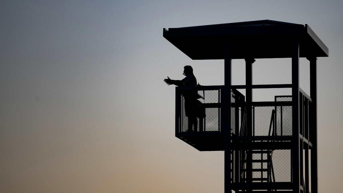 Silhouette of man in crow's nest above marching band field at dawn.