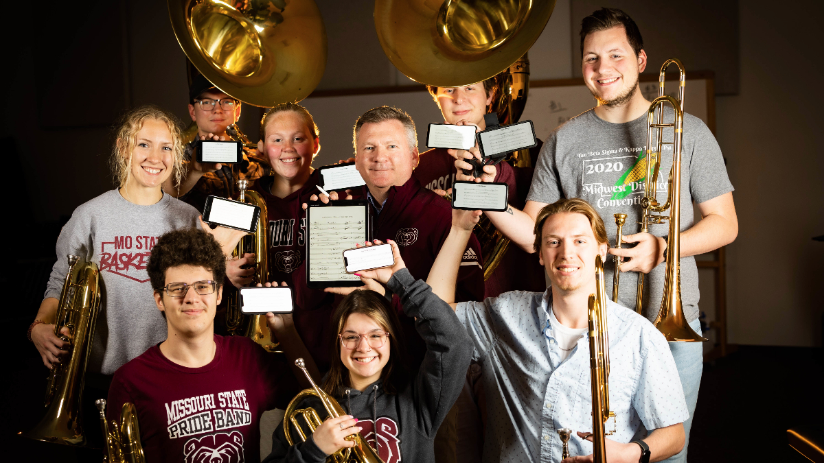 Brad Snow stands surrounded by band members displaying their instruments and coordinates.