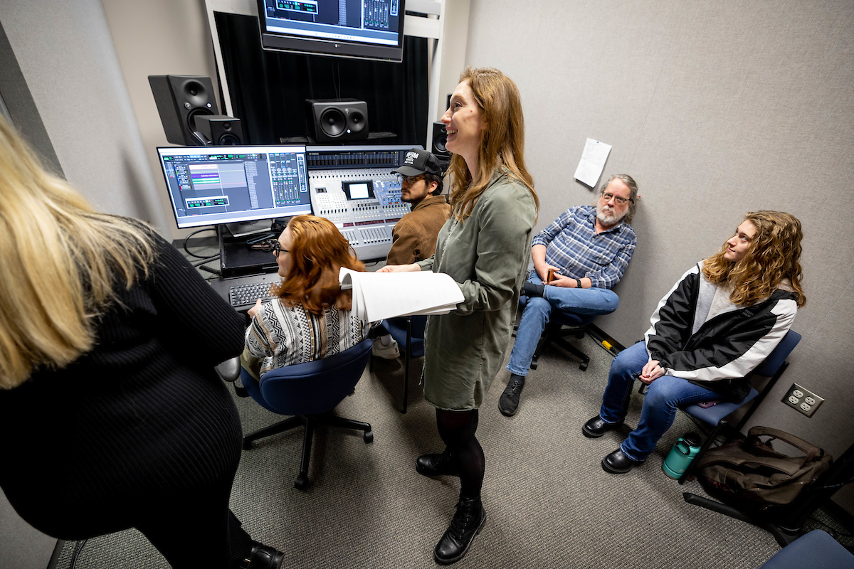 Christina Pippa listens to a vocal student sing from inside an audio recording booth. 