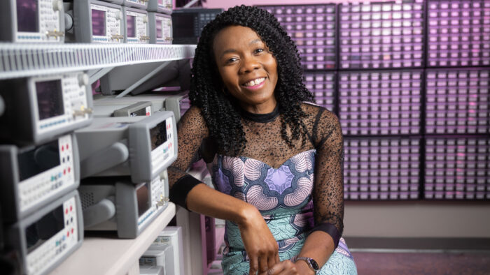 Tayo Obafemi-Ajayi sits in lab in front of a violet colored wall.