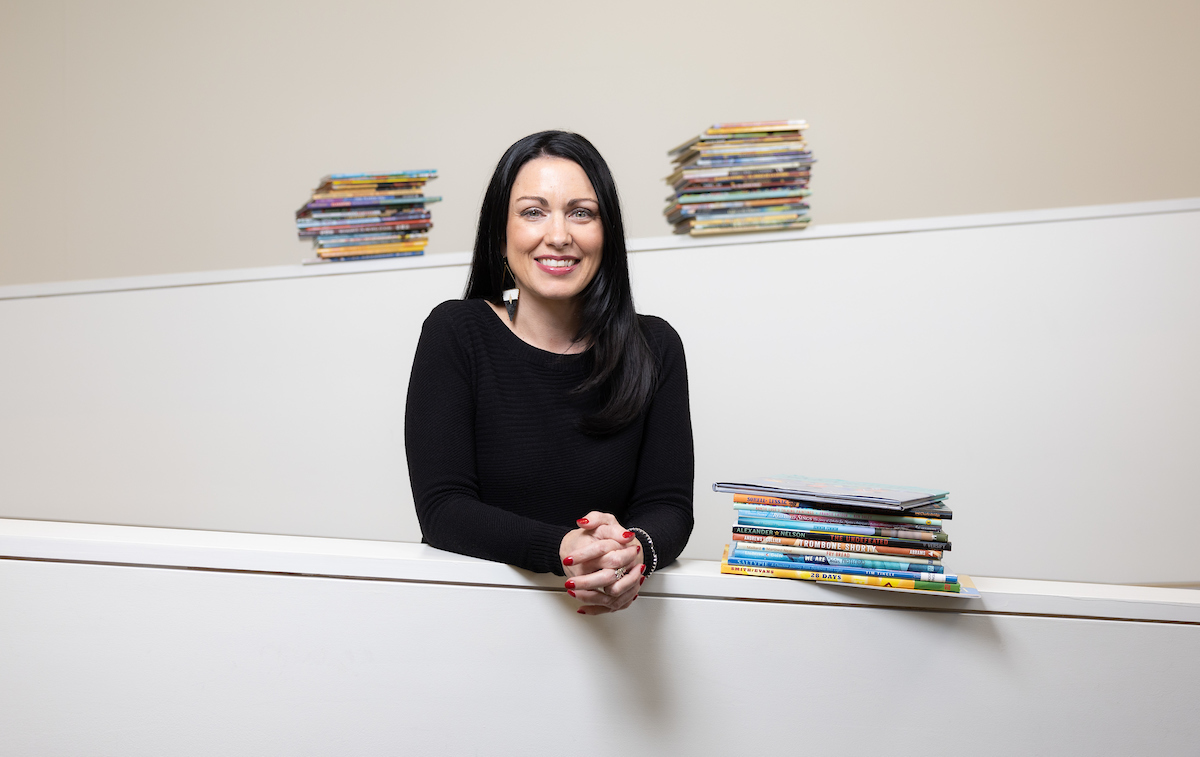 Dr. Kayla Lewis poses between colorful stacks of children's books.