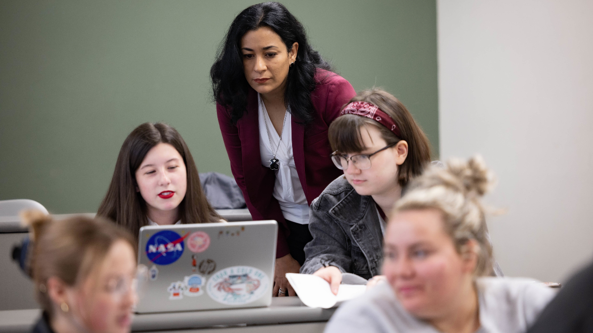 Judith Martinez looks over the shoulders of two female MIssouri State University students in classroom.