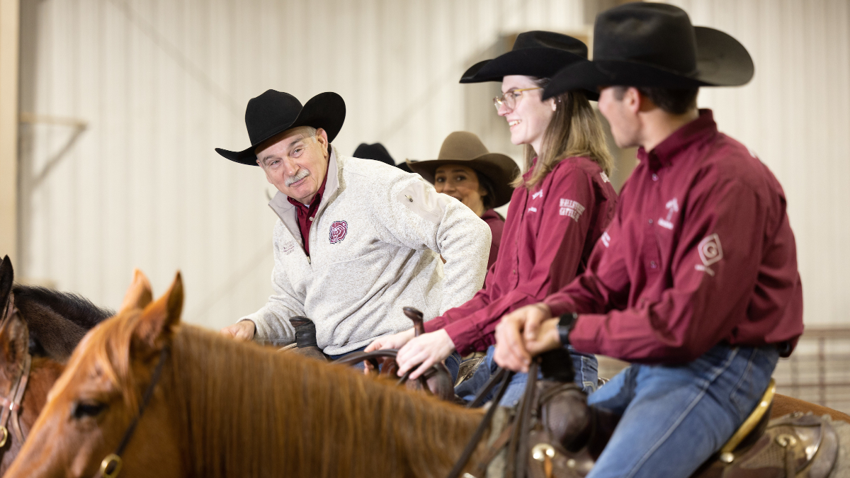 Gary Webb, and several students, sit on horseback in arena and talk.