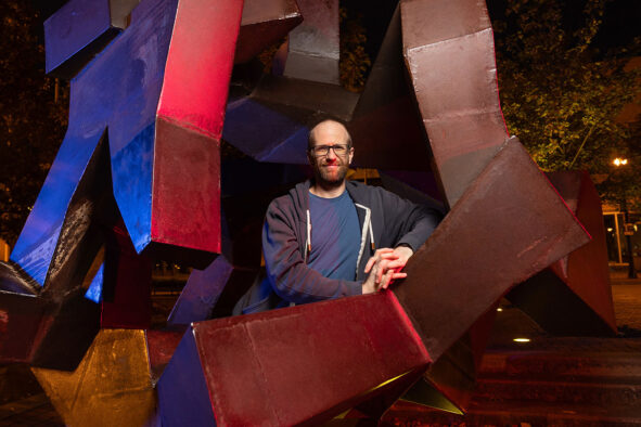 Posing for the camera, Dr. Steven Senger rests his arms on an outdoor geometric sculpture.