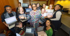 Dr. West cheerily grins as members of her faculty group gather around her for a picture while holding their laptops.