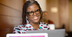 Dr. West sits in front of her laptop and smiles at her peers during a group discussion.