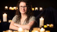 Erin Wehrman, an associate professor at Missouri State, crosses her arms while posing, surrounded by candles.