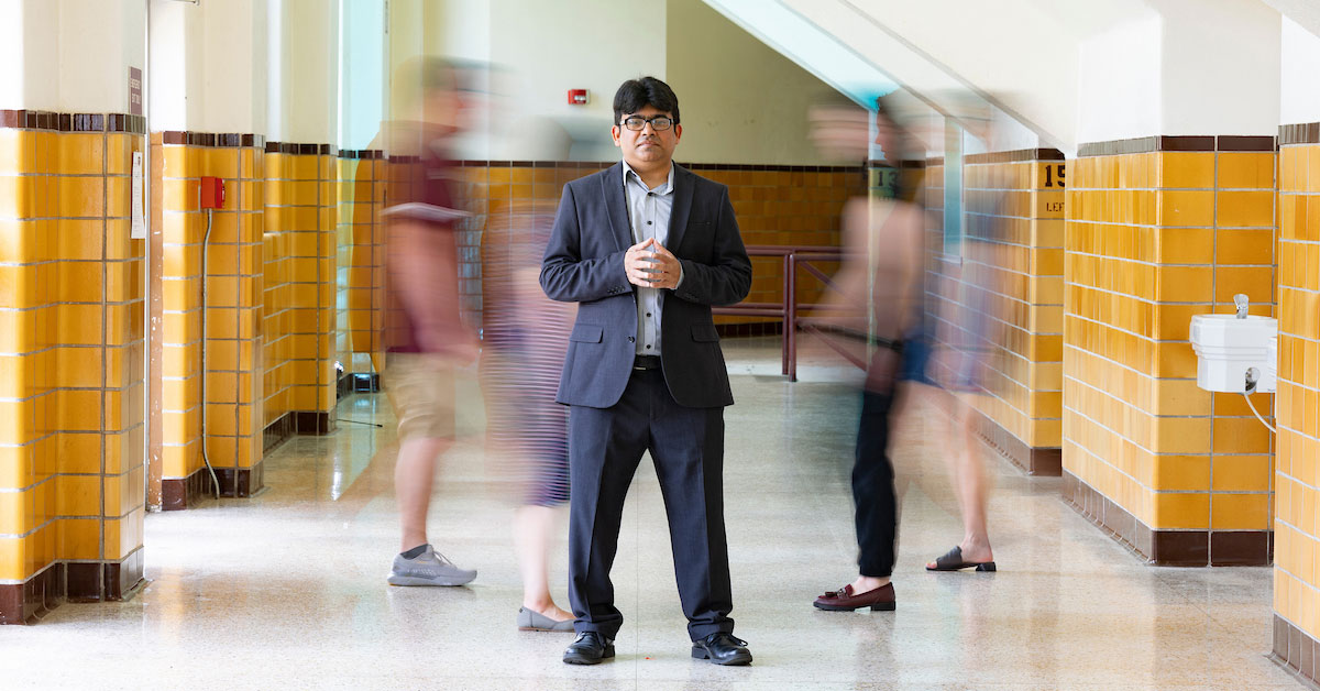 Dr. Muhammad Hassan Raza stands in the center of a hallway, as people blurrily move in the background.