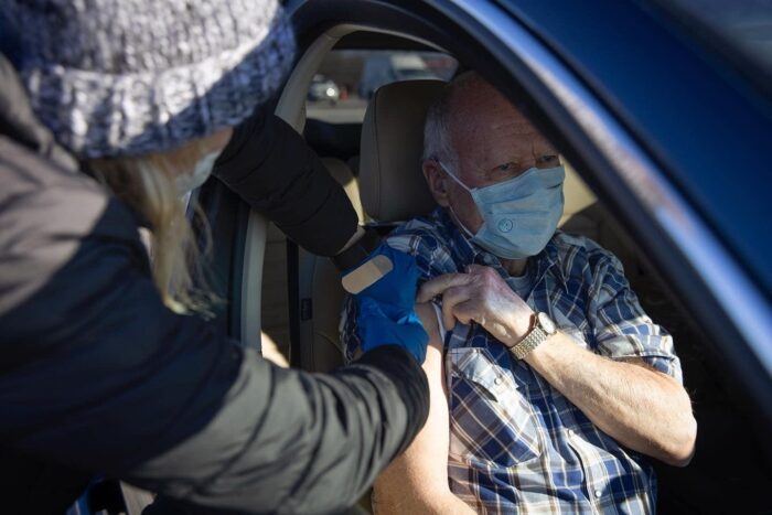 Someone giving an vaccine to an old man in their car