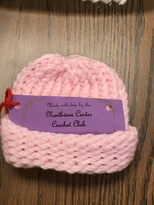 A pink crocheted stocking cap with attached paper tag reading, Made with love by the Northview Center Crochet Club