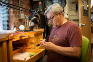 MSU 62 student, Ricky sits at a work bench making small rings. 