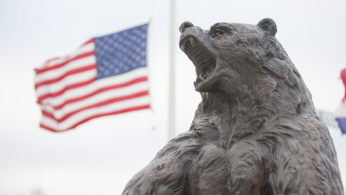 The Plaster Stadium Bear Statue with the U.S. Flag at half-staff in the background.