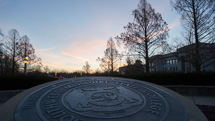 University seal at sunrise in front of Carrington Hall