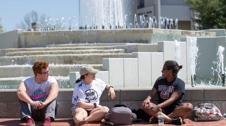 Three students sit by fountain.