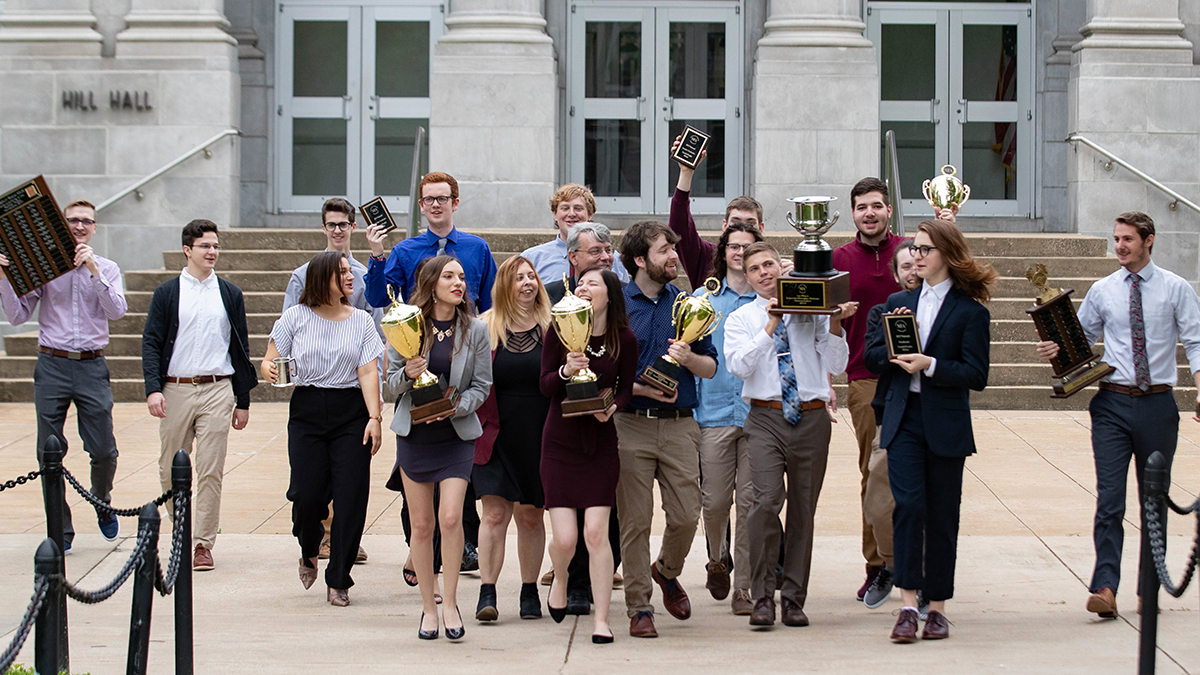 Debate team with awards in front of Hill Hall
