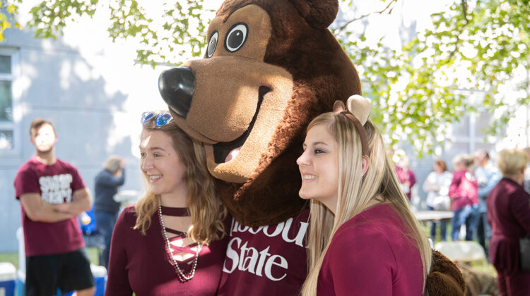 Two female student pose with Boomer in Bearfest Village