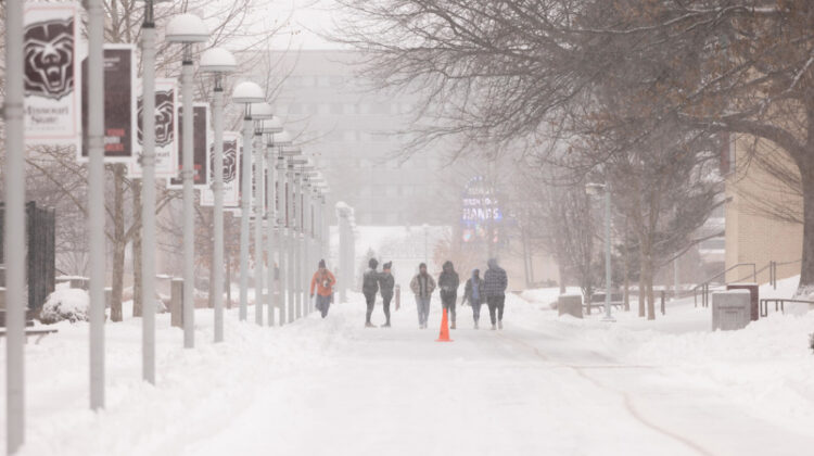 Students walk along campus sidewalks during snowstorm.