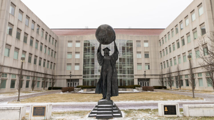 Citizen Scholar statue stands in front of a snow-capped Strong Hall.