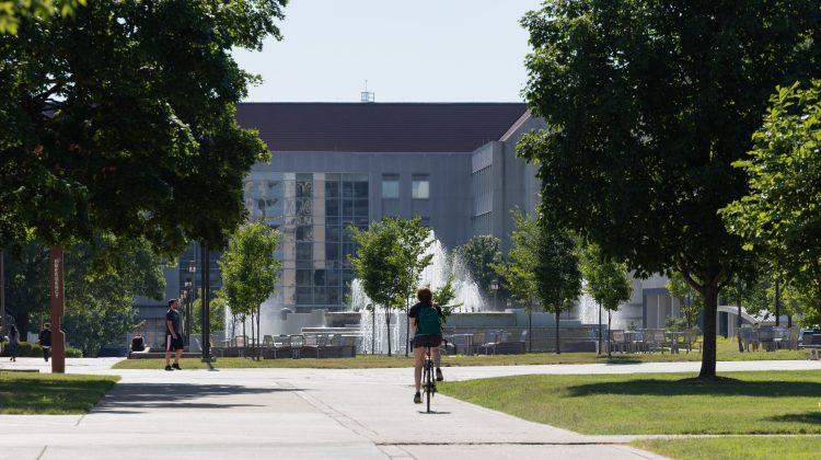 A student rides a bike on a sunny day on campus