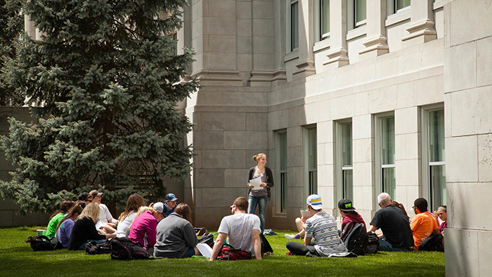 Professor teaching a group of students, who are seated on the green outside Missouri State University's Carrington Hall
