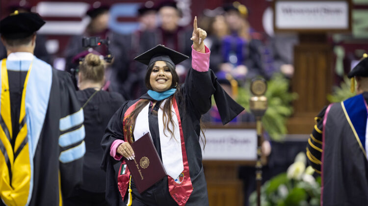 A graduate at commencement, pointing in celebration of her degree
