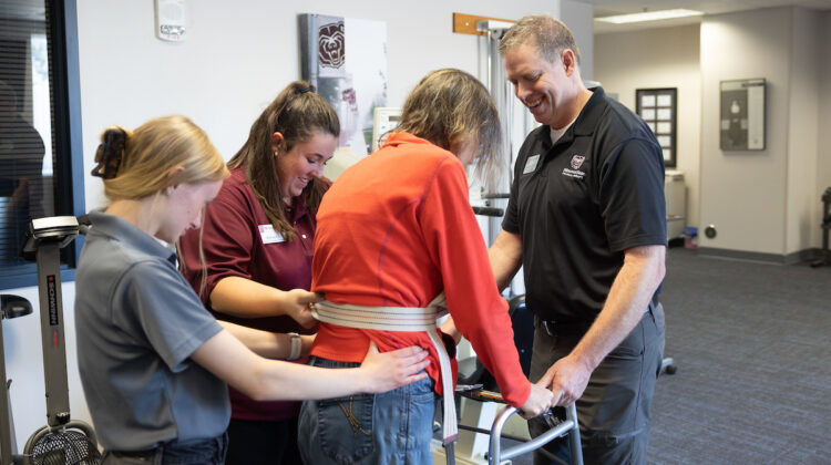 Missouri State faculty and students help someone use a walker in the physical therapy clinic