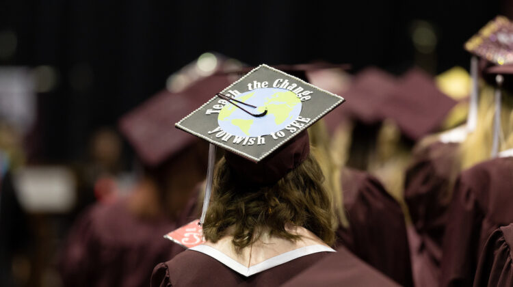 Closeup of a graduate's mortarboard, which reads: "Teach the change you wish to see."