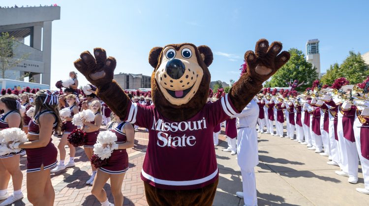 Missouri State's mascot, Boomer Bear, waving in front of members of the Pride Band.