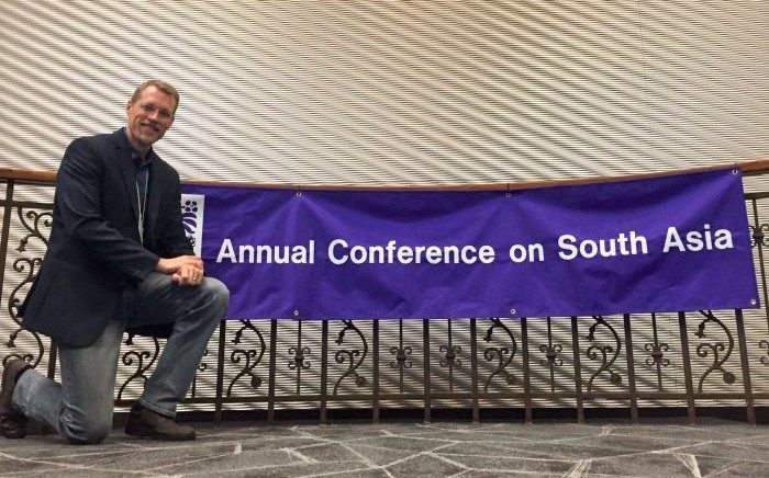 Photo of Dr. Matt Kuiper in front of the banner, "Annual Conference on South Asia"
